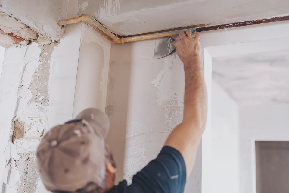 Plasterer utilisant une torche de finition pour lisser un nouveau plâtre à la surface d'un mur à l'intérieur d'une maison pendant les travaux de rénovation ou de construction